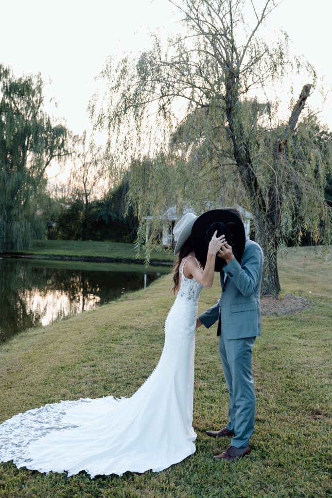 Bride and groom kiss behind cowboy hat outside