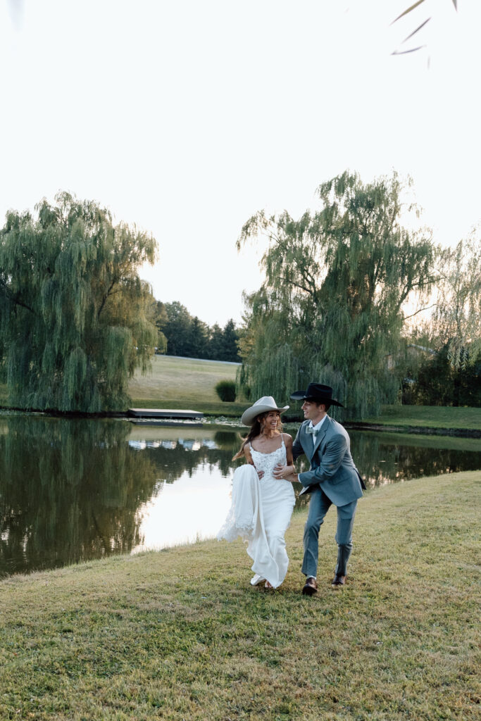 Bride and groom dance near lake with lush greenery surrounding