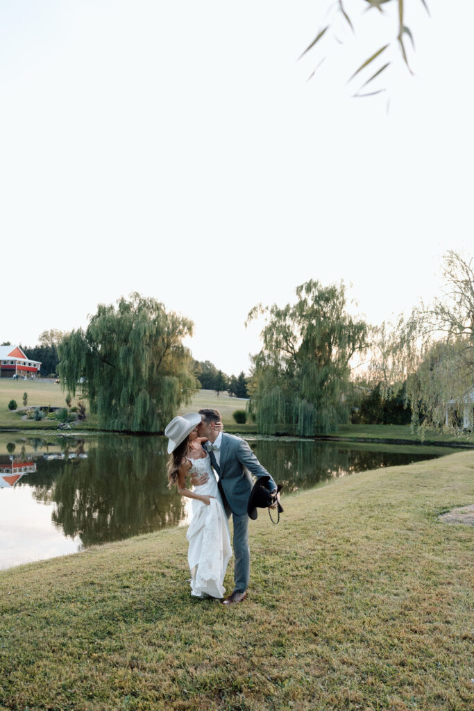 Bride and groom kiss next to lake outside