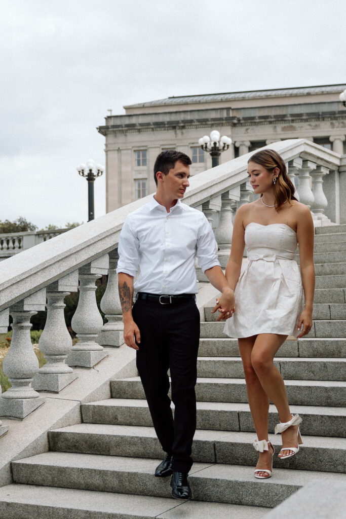 Engaged couple descend luxurious steps outside luxury engagement photos