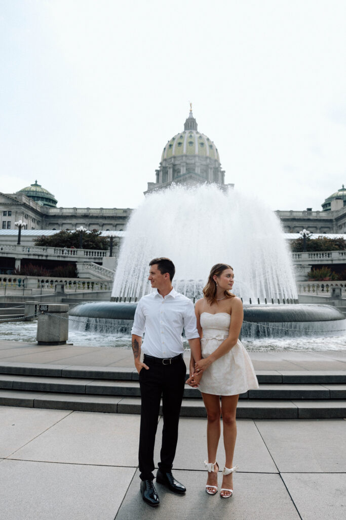 Engaged couple gaze outside in front of beautiful fountain at the captiol luxury engagement photos