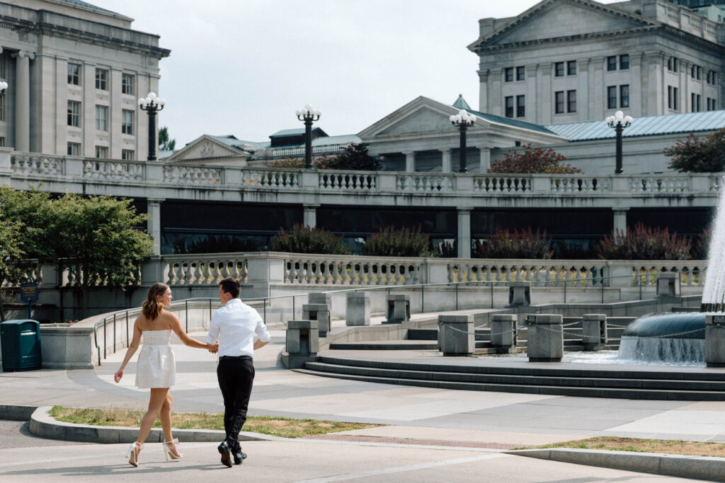 Engaged couple walk around Pennsylvania State Capitol building holding hands