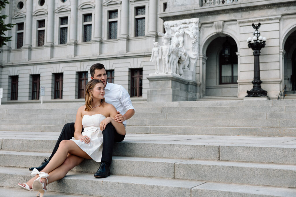 Engaged couple sit on the steps of the State Capitol in Pennsylvania