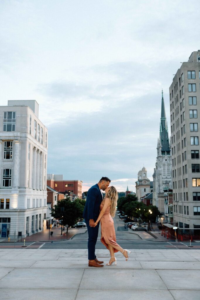 A couple kissing downtown at the PA State Capital with the city in the background.