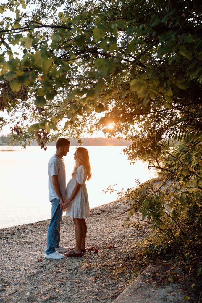 Couple at sunset by a lake and greenery at Cordorus State Park posing for their engagement photographer. 