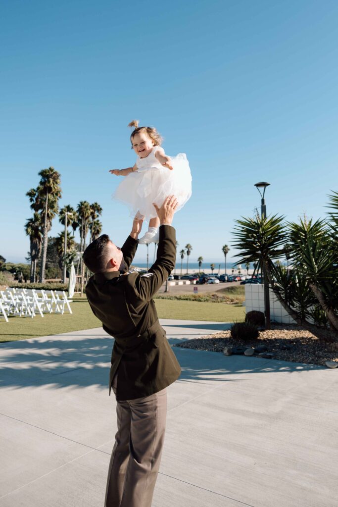 Groom throwing his daughter up into the air as she smiles.