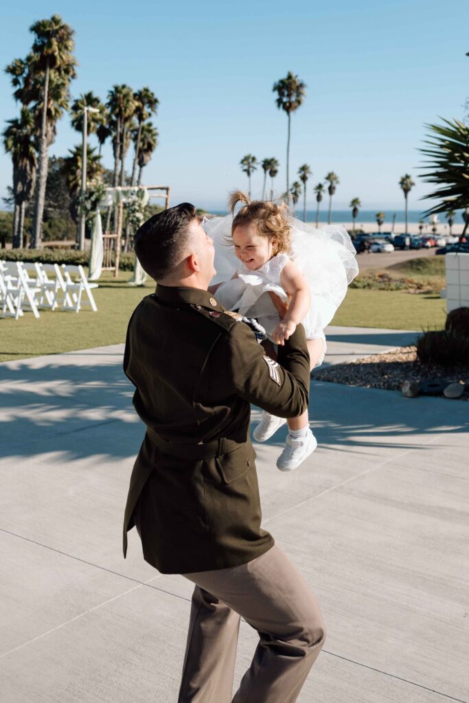 Groom about to throw his daughter in the air as she laughs. 