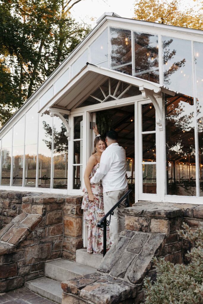 Engaged couple in the doorway of the greenhouse laughing and smiling.