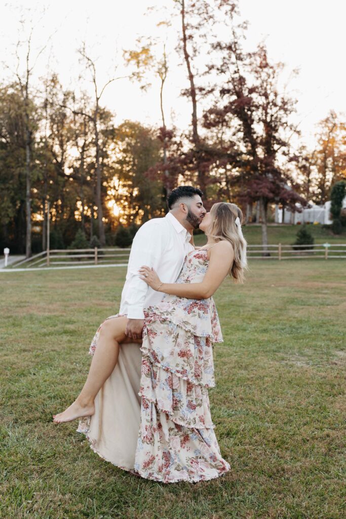 An engaged couple dipping for a kiss in an open field. 