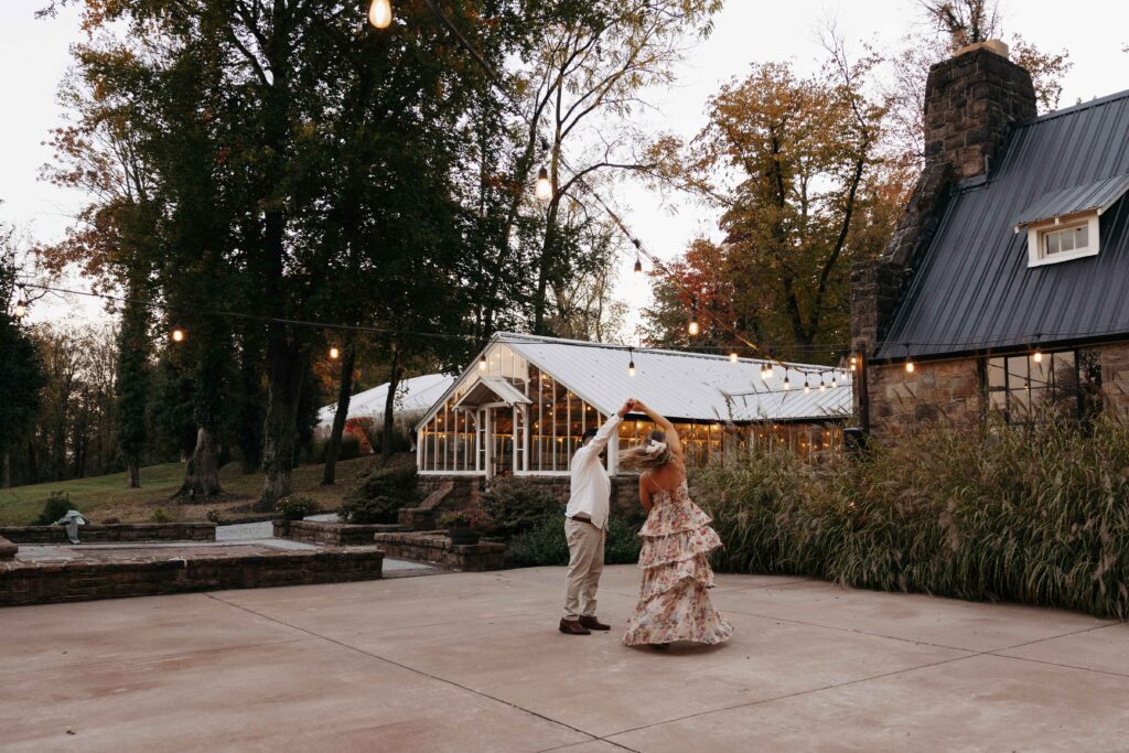 A man spinning his fiancee as they dance in a courtyard at their engagement photoshoot.