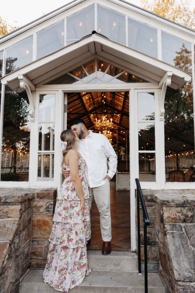 Couple kissing during their engagement photoshoot in the doorway of the greenhouse.