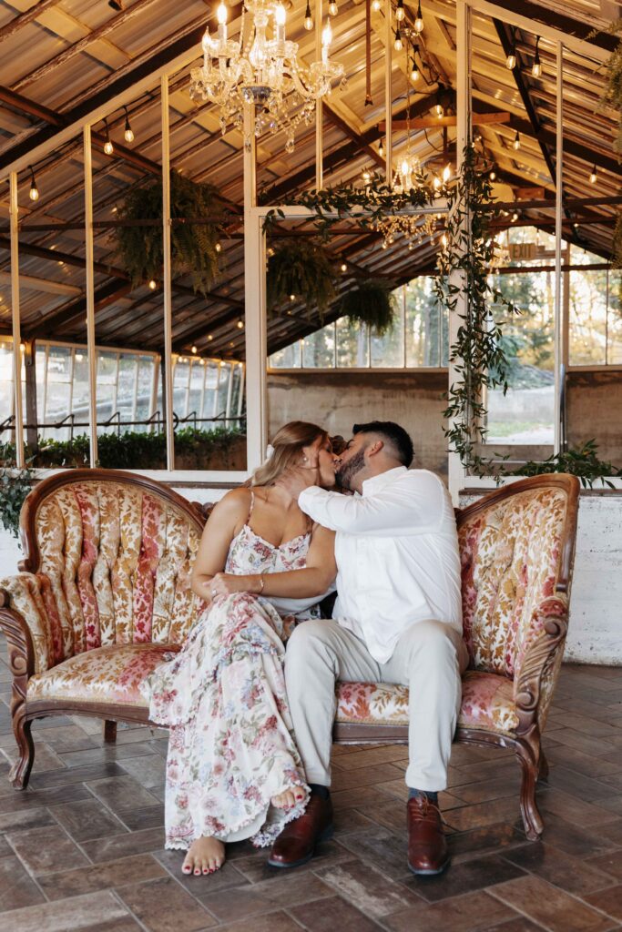 An engagement photoshoot of a couple kissing on a vintage couch.