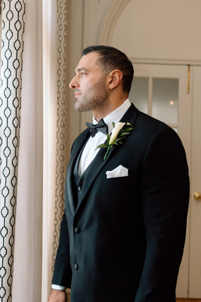 Groom looking out the window in his wedding suit.