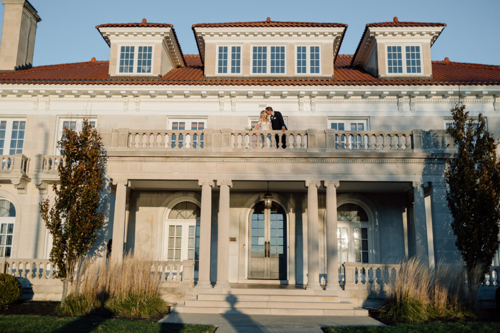 Elegant wedding photos at King Mansion. The bride and groom are kissing on the balcony.