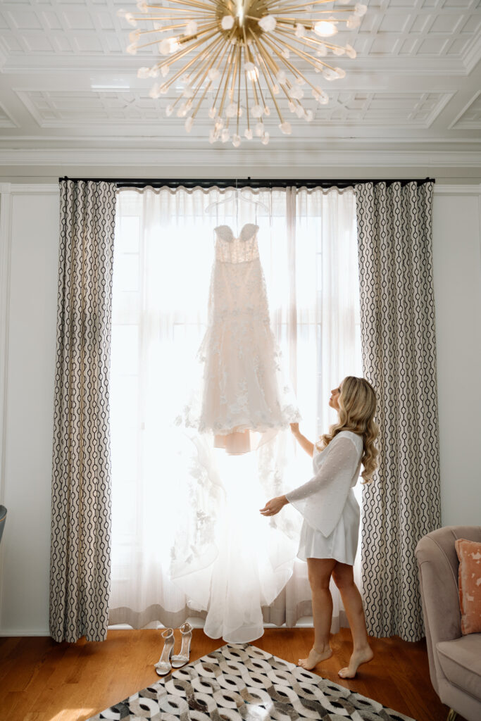 Bride in a robe looking up at her wedding dress handing.