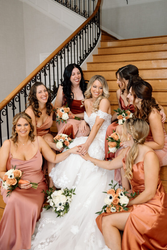 The bride and bridesmaids sitting on the stairs, smiling at one another.