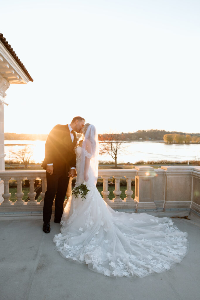 The newlyweds kissing during golden hour on the terrace overlooking the river at King Mansion in PA.