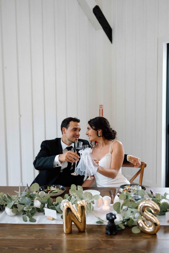 Bride and groom holding up their glasses at their sweetheart table.   