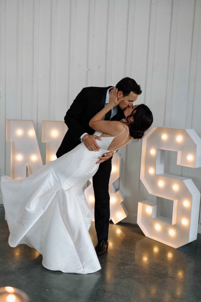 Bride and groom kissing in front of a light up sign at The Lookout at Hope Lake.