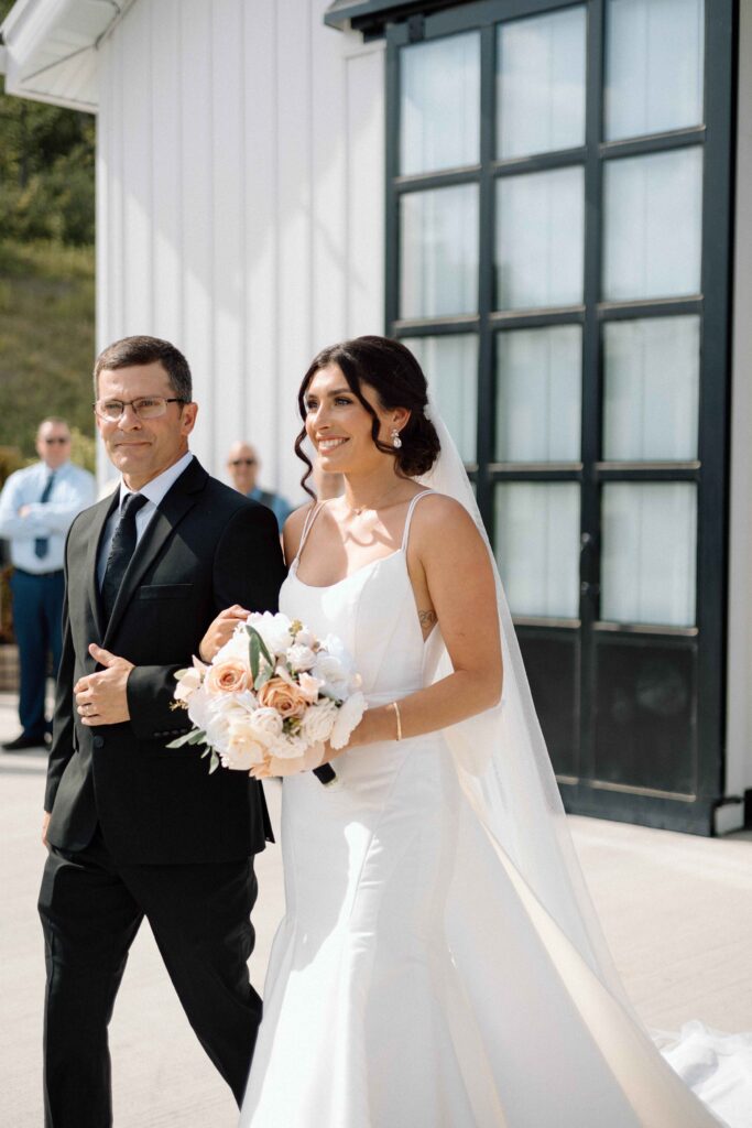 Bride smiling at the groom as she walks down the aisle with her father. 