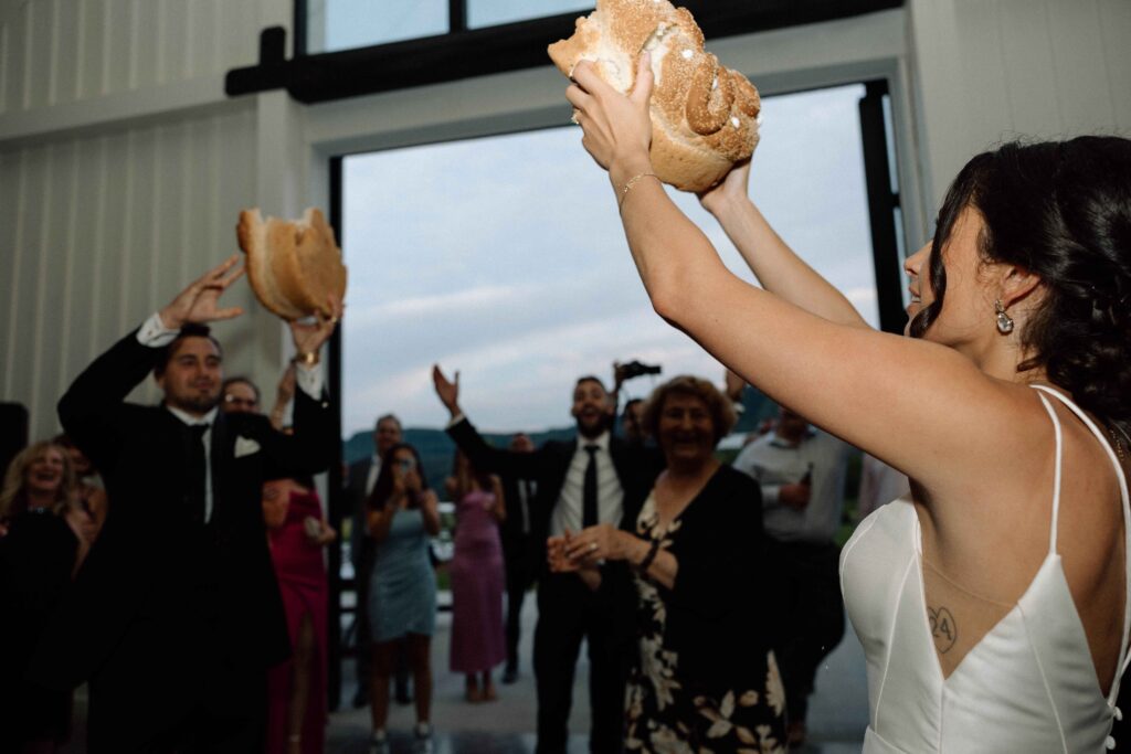 Bride and groom breaking bread at their reception with guests cheering. 