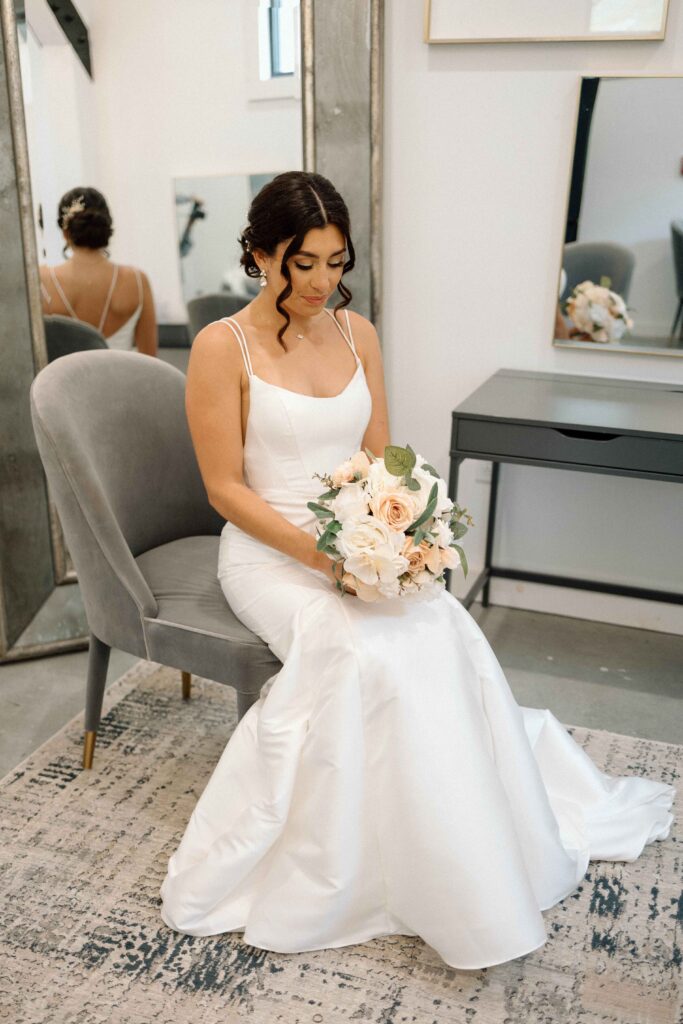 Bride sitting in her getting ready suite in her dress and holding her bouquet. 