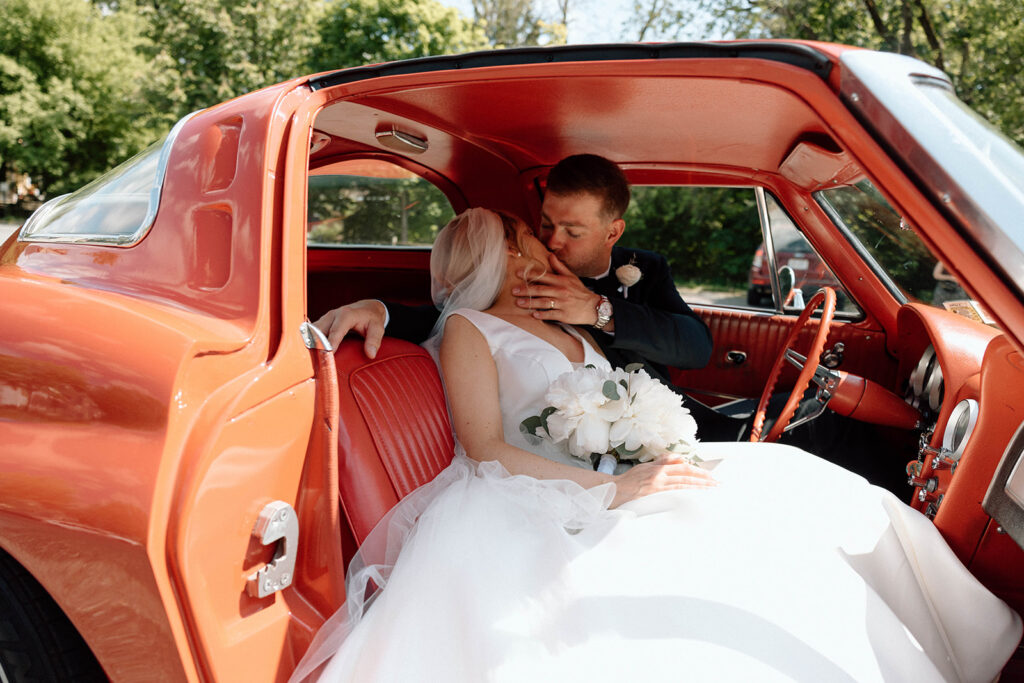 Newlyweds kissing in a vintage Camaro after their wedding ceremony.