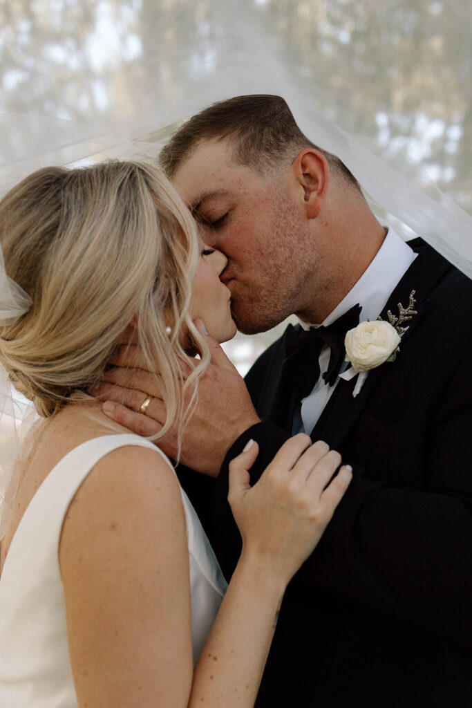 Bride and groom kissing romantically under the brides veil.