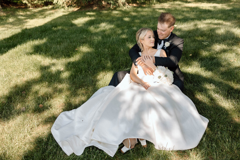 Bride and groom laying in the grass, holding each other.