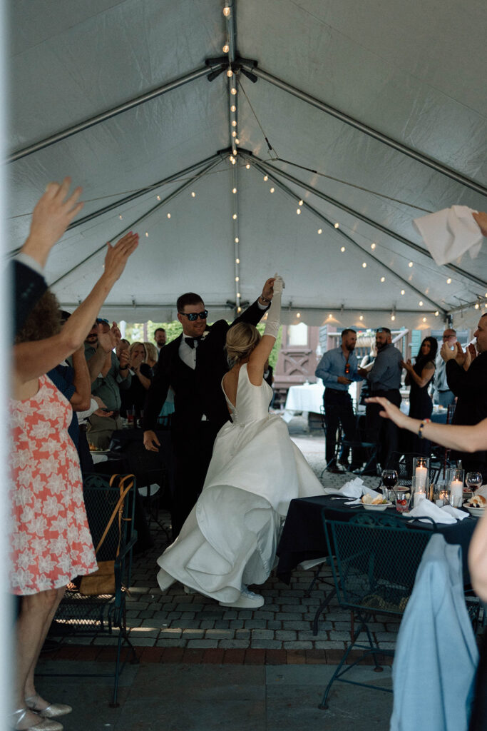 Bride and groom dancing as they enter their wedding reception while guests clap.