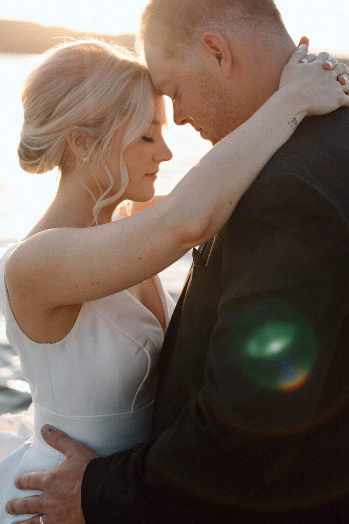 Bride and groom holding one another on a dock by a lake.