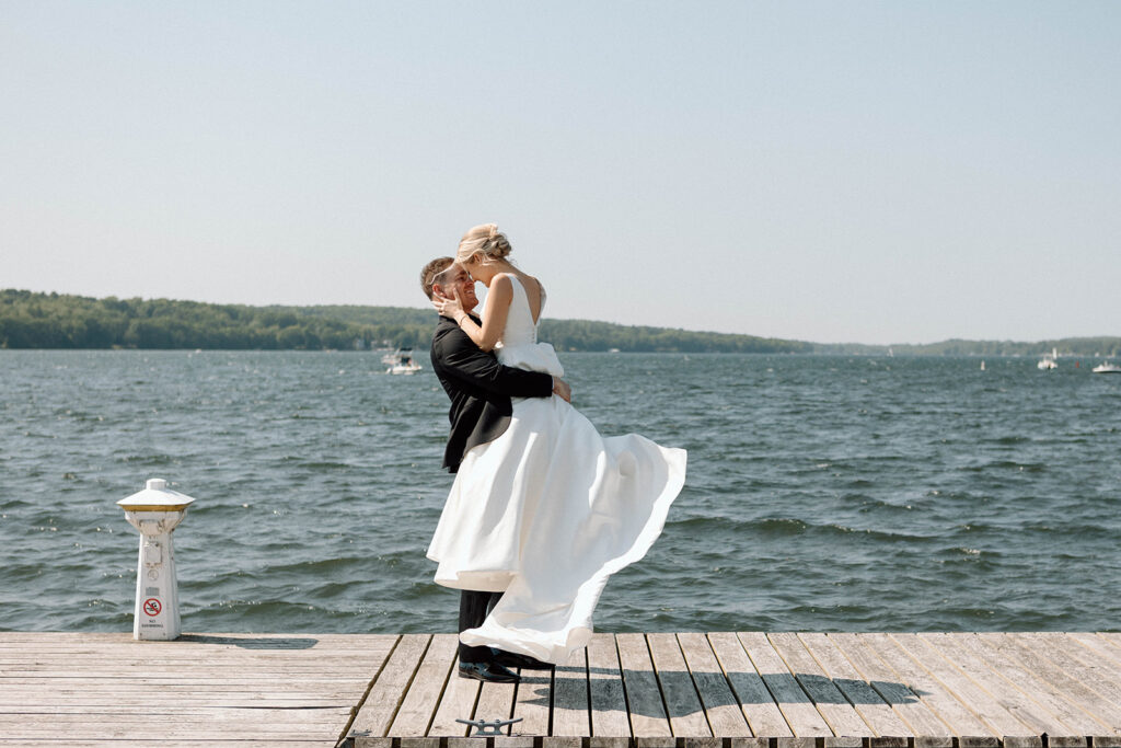 Groom spinning his wife romantically on a dock by a lake after their wedding ceremony. 