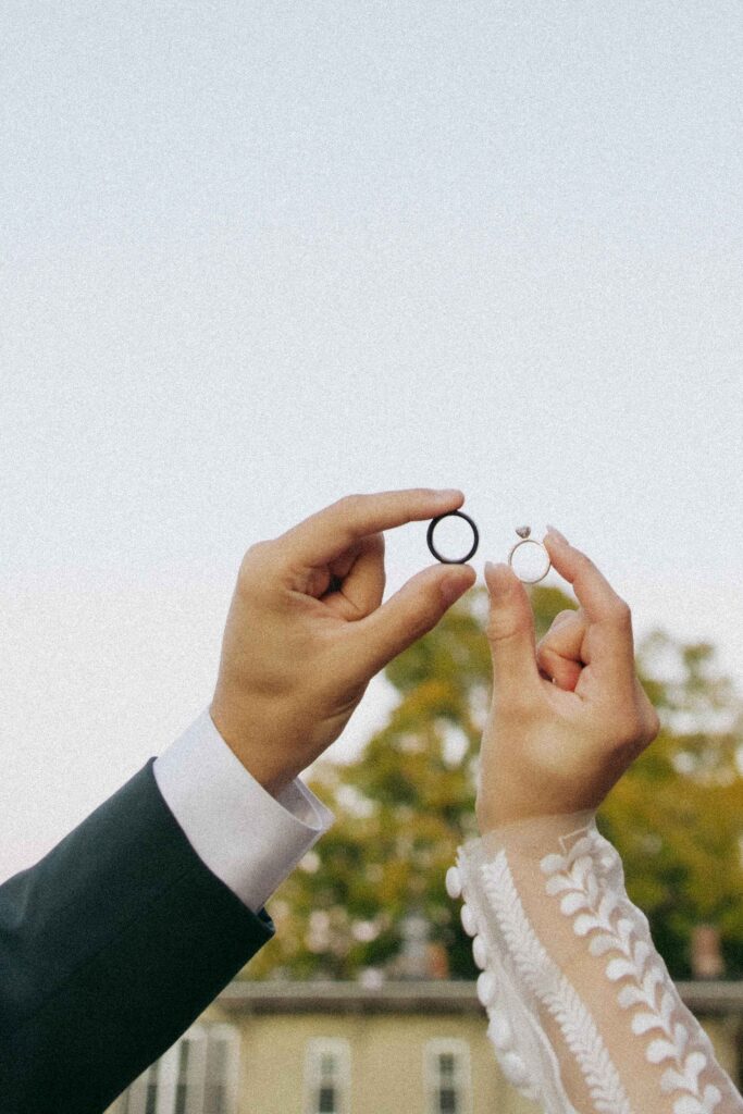 Bride and groom holding their wedding rings up in the sky. 