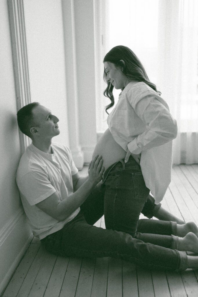 Husband and wife sitting on the floor while the husband rubs his wife's baby belly.