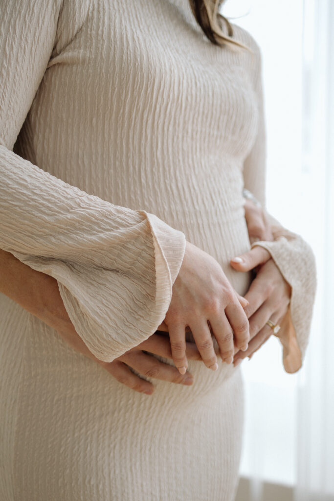 Close up of a woman's pregnant belly with her husband's arms wrapped around her. 