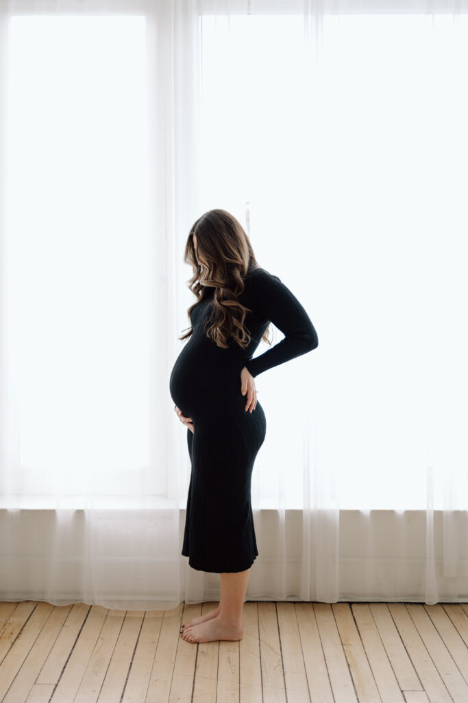 Maternity photos of the mom to be holding her belly by a window.