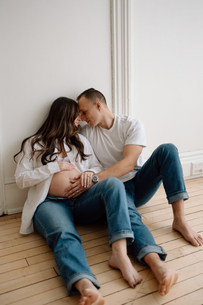 Husband and wife sitting on the floor and holding the wife's baby belly.