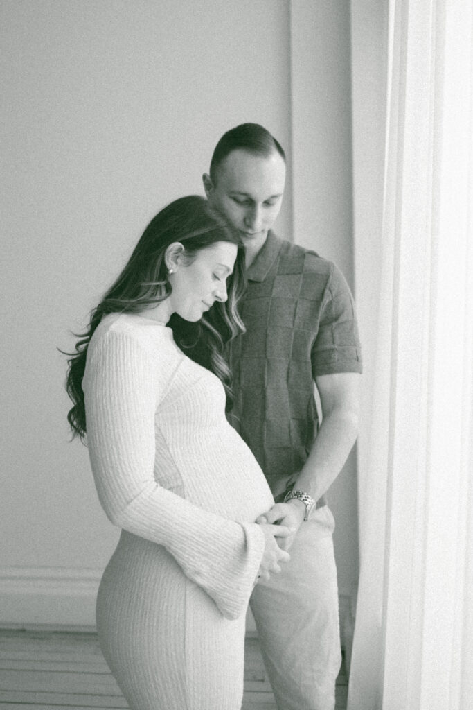 Film maternity photos of husband holding his pregnant wife.