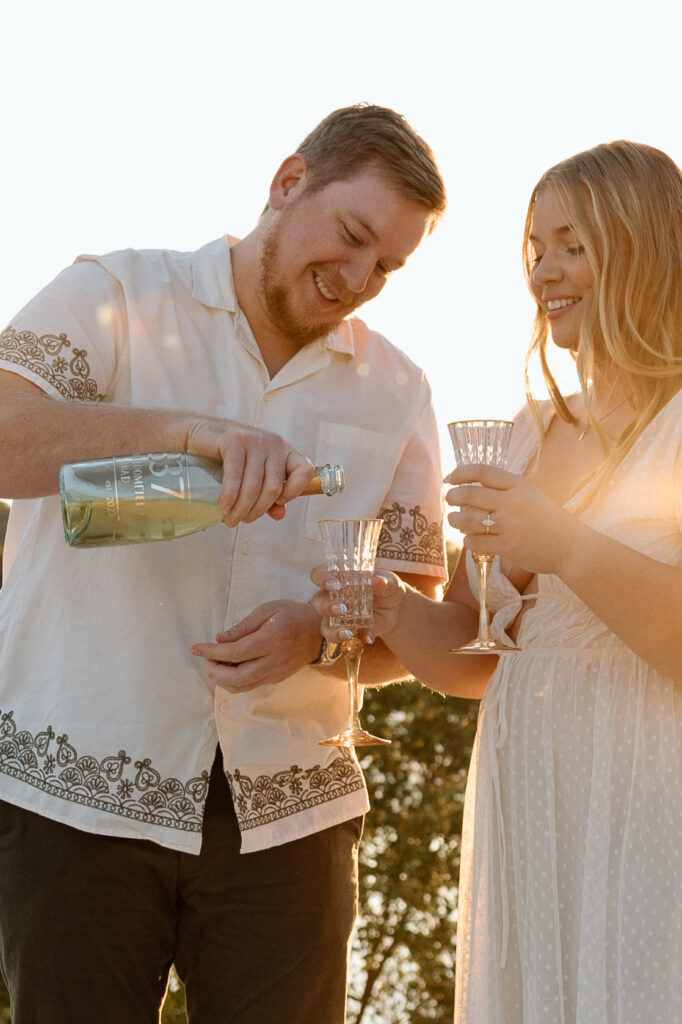 Engagement photo poses of a couple pouring champagne during golden hour. 