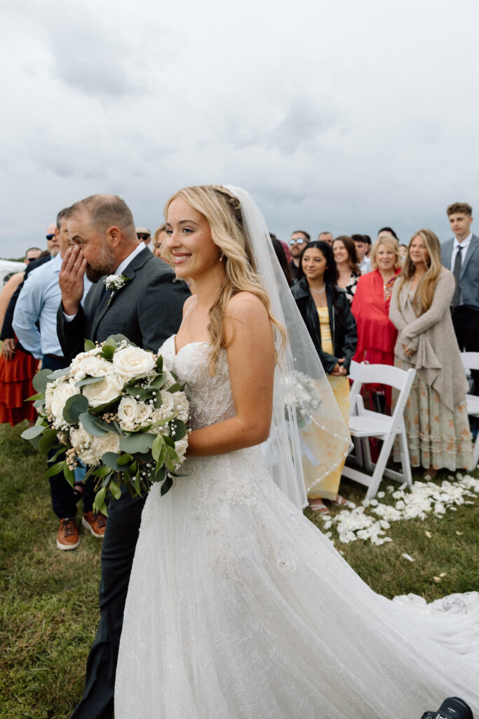Bride smiling really big as she walks down the aisle. 