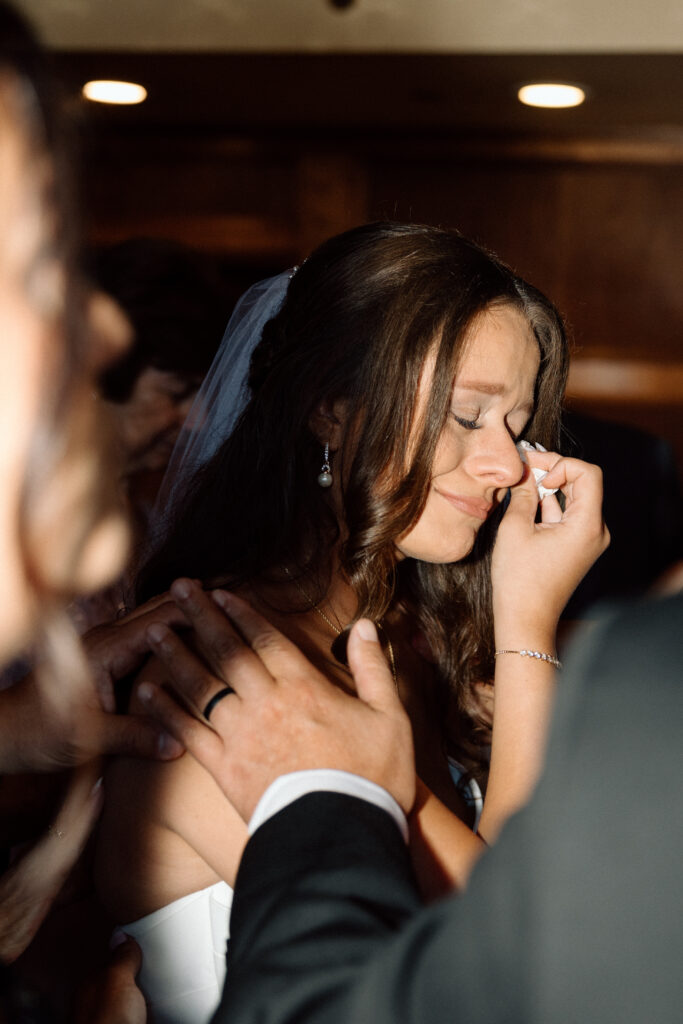 Bride crying while family prays over her before her luxury wedding ceremony. 