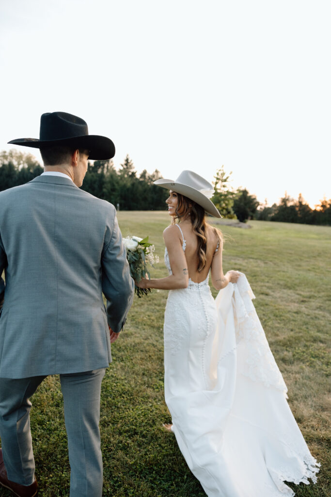 Bride and groom walking in a field with cowboy hats on. 