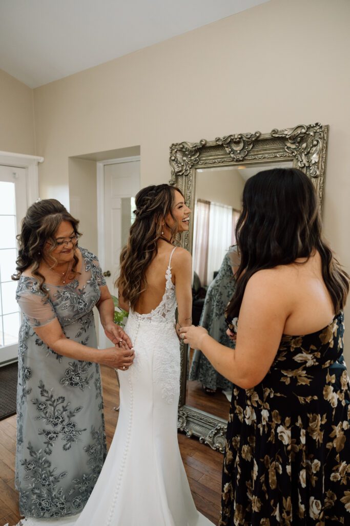 Bride laughing while her family helps her into her wedding dress.