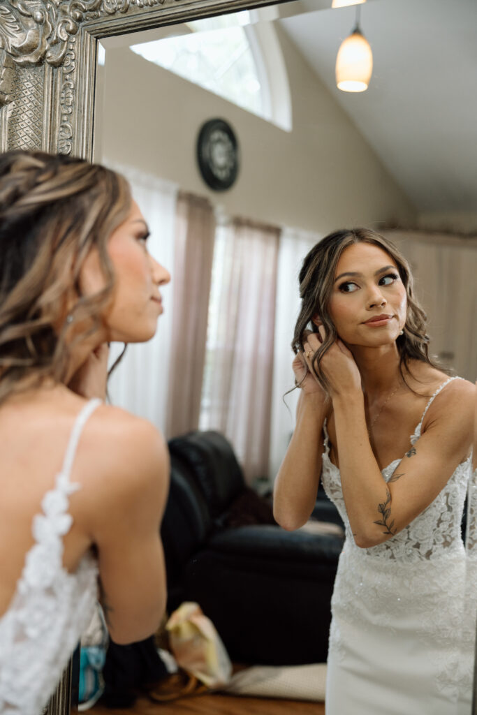 Bride putting on earrings in the mirror.