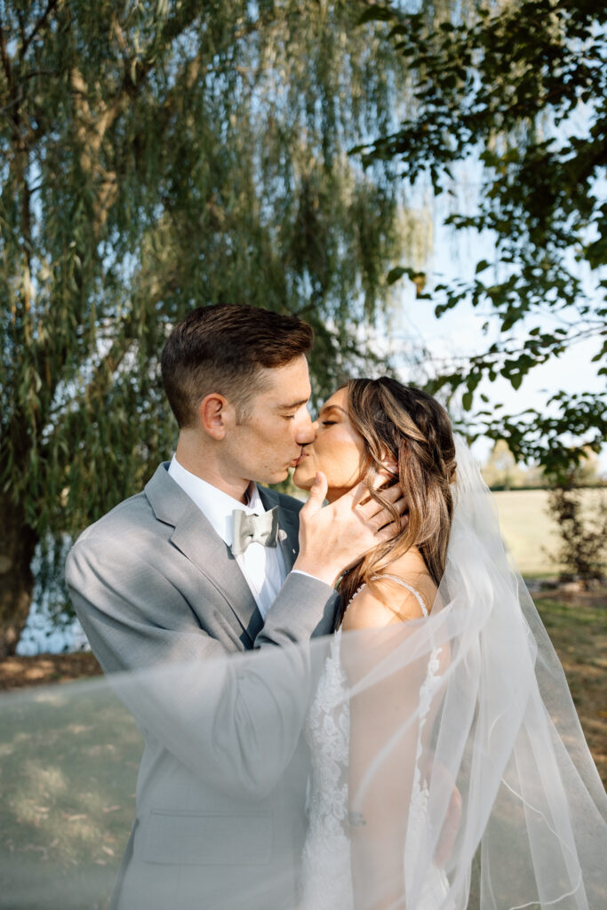 Newlyweds kissing passionately while the bride's veil flows in the wind.