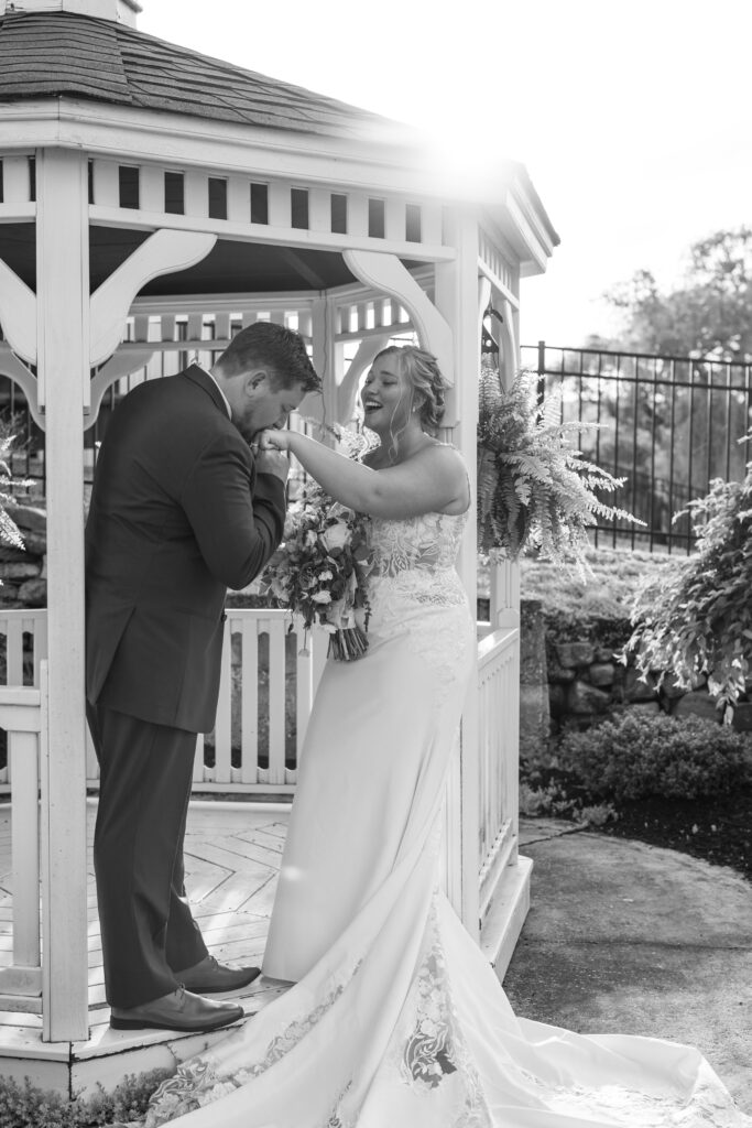 Groom kissing his bride's hand in a gazebo. 
