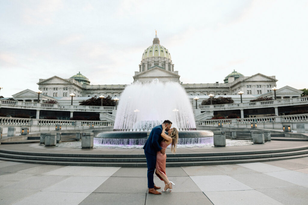 Newly engaged couple kissing at the PA State Capital in their engagement session outfits. 