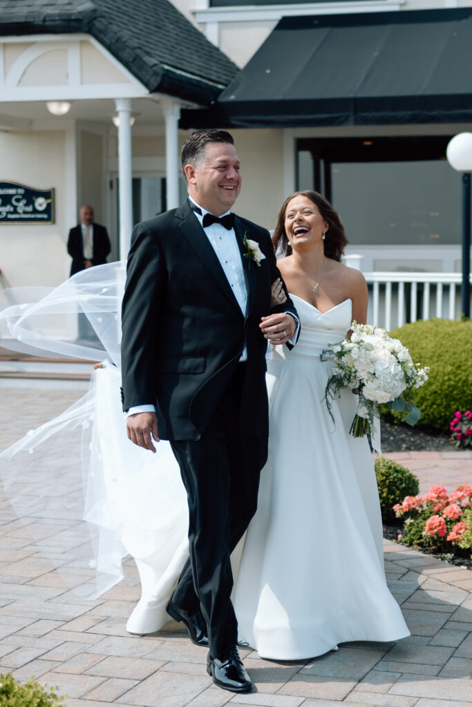 Documentary style wedding photography of a father walking his daughter down the aisle while smiling and laughing. 