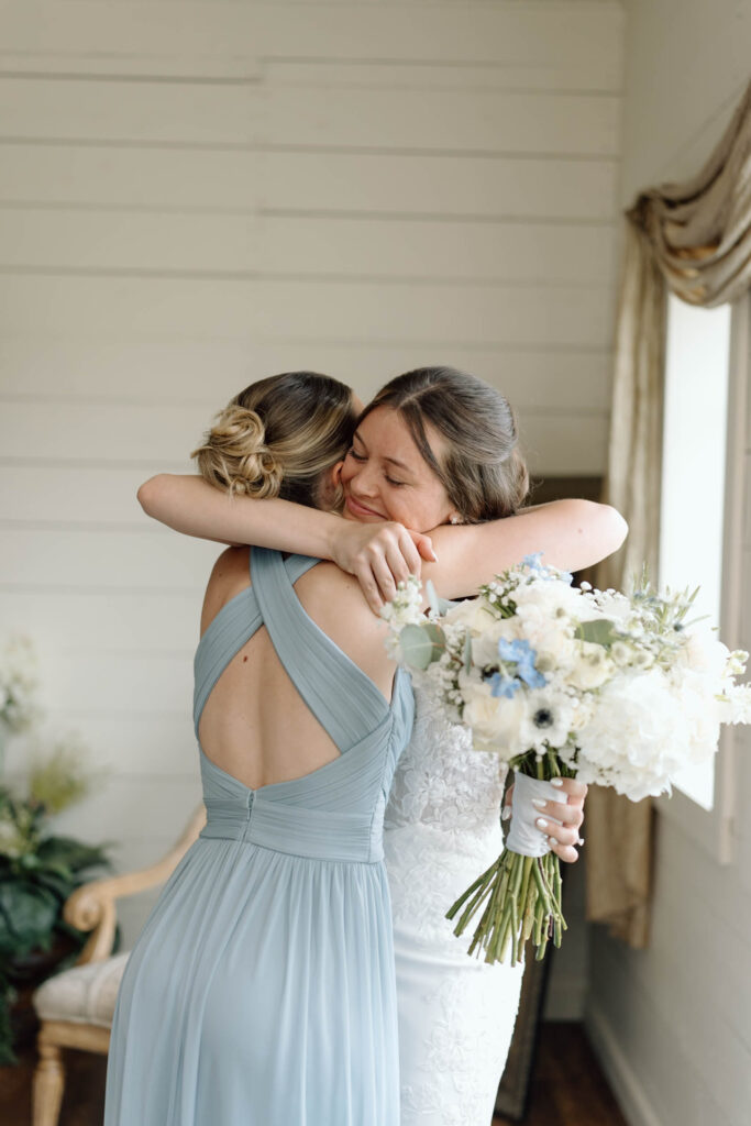 Documentary style wedding photography of a bride hugging her bridesmaid and smiling. 