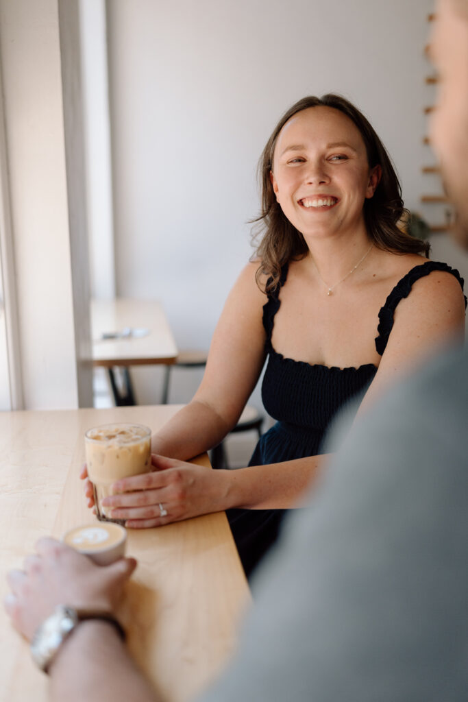 The best engagement photo locations at a coffee shop where the bride to be is smiling at her fiance.
